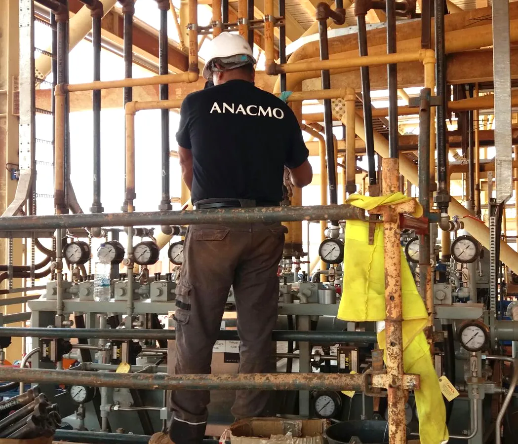 Technicien ANACMO relevant des mesures sur une rampe de manomètres depuis un échafaudage